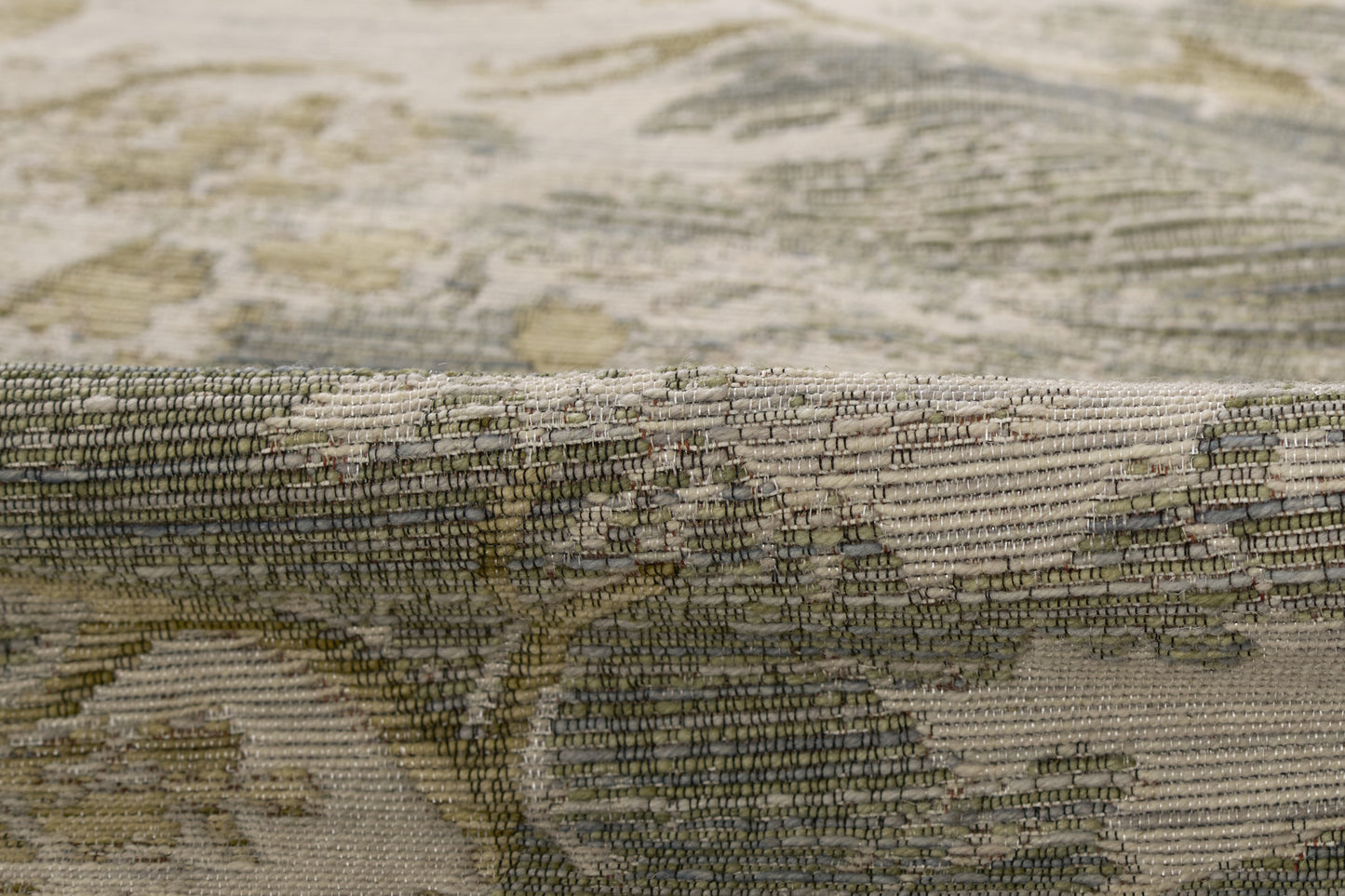 Beige-brown ornate rug with sage green and gray floral pattern; rolled edge shows tight woven texture
