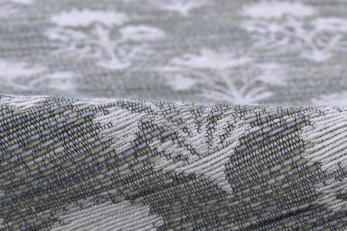 Close-up of a gray-blue woven rug with white damask pattern, textured weave, and folded edge.