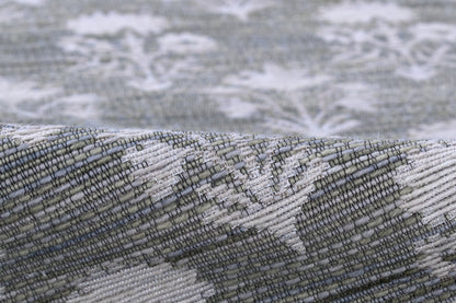 Blue-gray woven rug with white damask pattern and rolled edge, textured jacquard style.