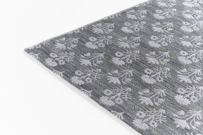 Gray-blue woven rug with white floral pattern; textured jacquard weave, corner edge visible.