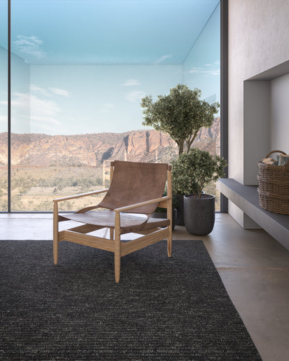 Oak-framed mid-century lounge chair with tan leather seat in a modern room, large glass wall and potted plant.