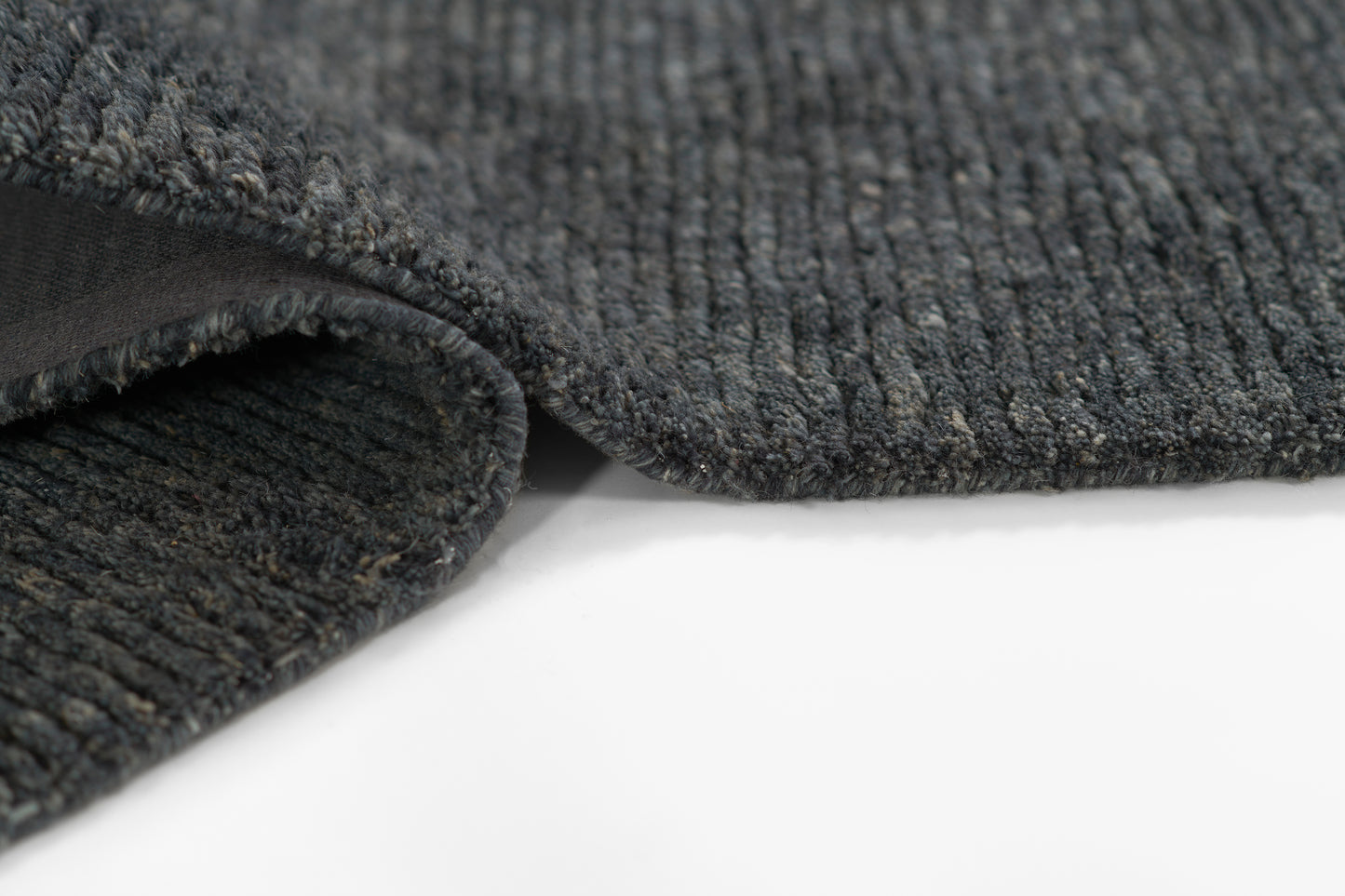 Dark charcoal loop-pile rug with textured fibers and a folded edge.