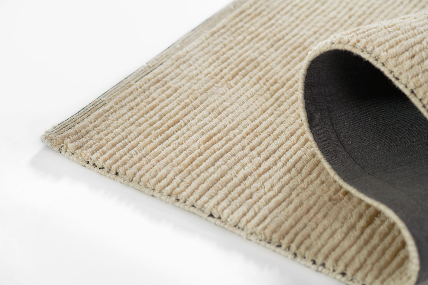 Beige ribbed rug with corduroy texture and black backing, curved corner revealing underside.