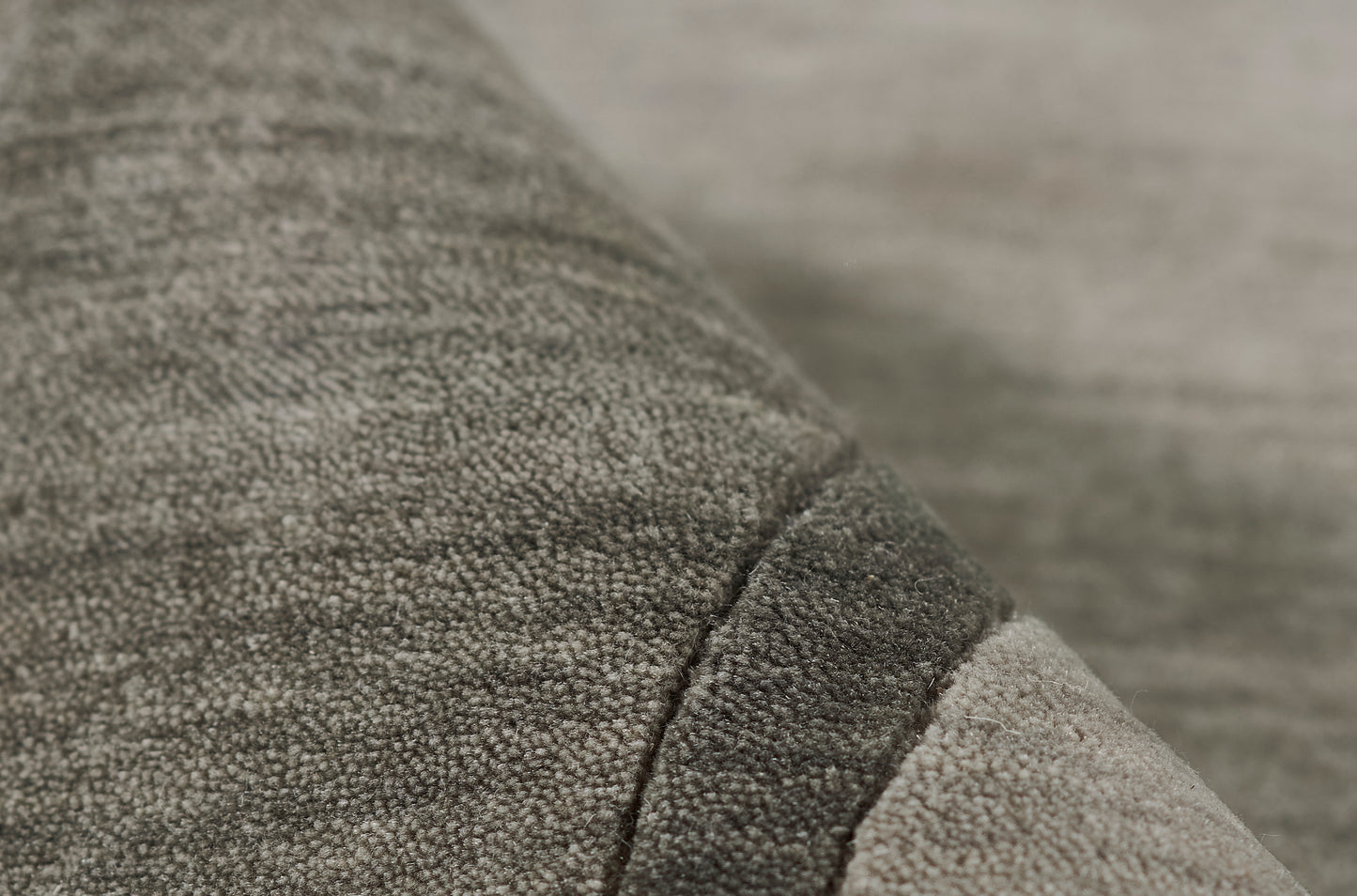 Close-up of gray boucle fabric with a dark seam and lighter edge, plush cozy textile.