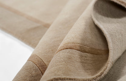 Beige suede-like fabric close-up with soft nap and folded edge, cozy throw or upholstery swatch.