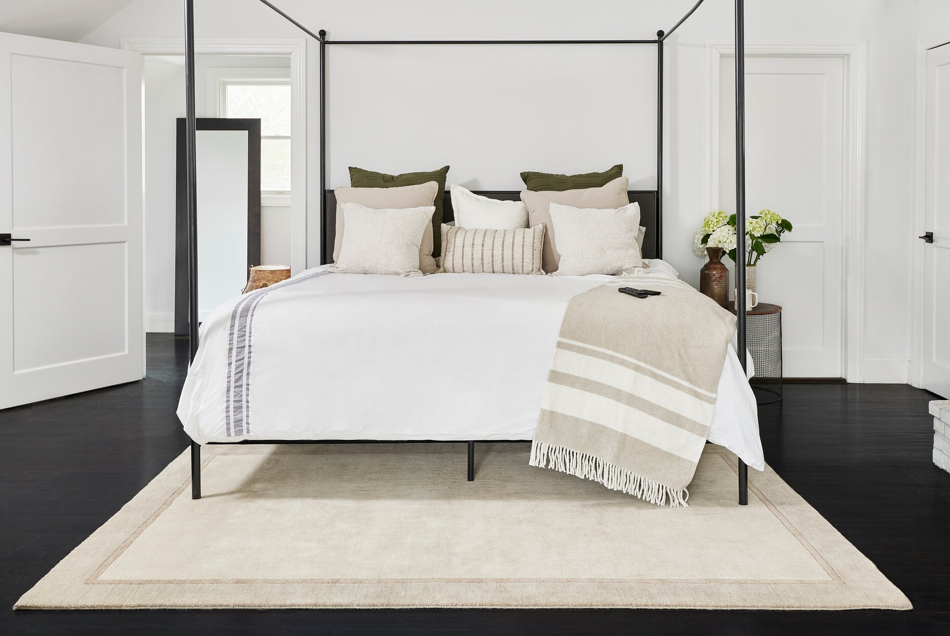 Black metal canopy bed with white bedding, beige throw, & neutral pillows in a bright modern bedroom.