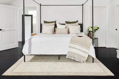 Black metal canopy bed with white bedding, beige throw, & neutral pillows in a bright modern bedroom.