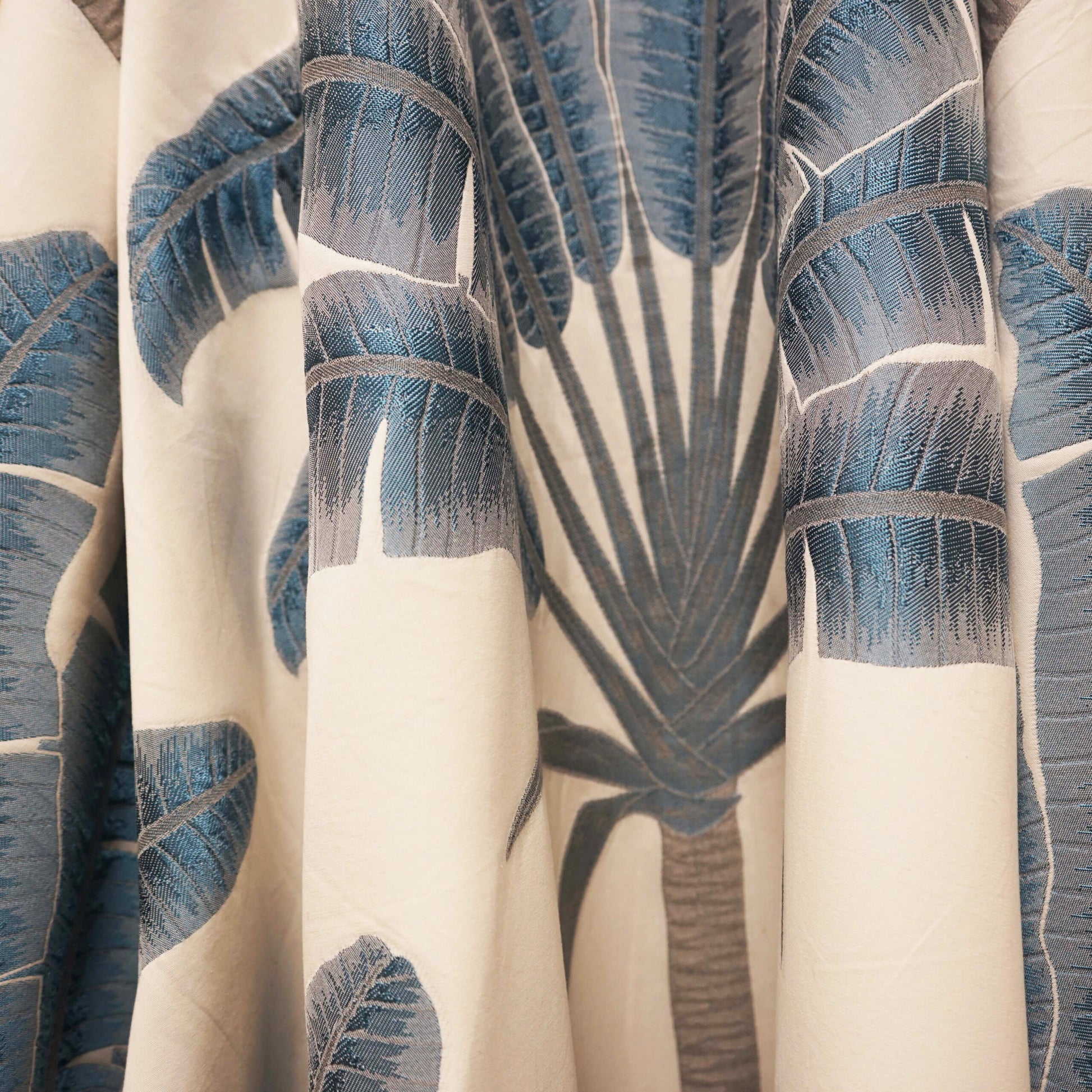 Cream fabric with blue palm leaf print, tropical botanical pattern, soft drape, ideal for curtains or throws.