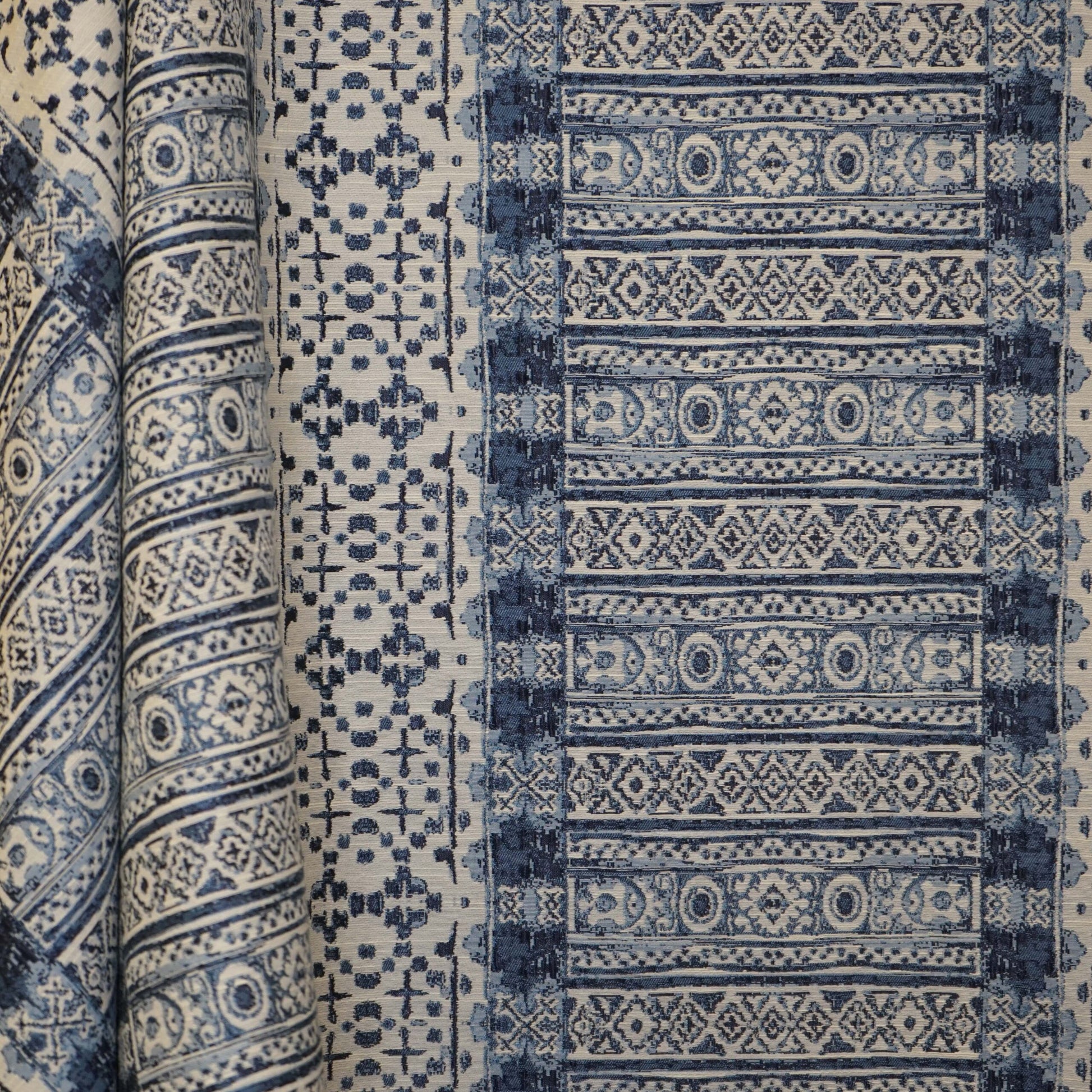 Indigo blue and white woven textile with repeating geometric and floral motifs, rolled for display.