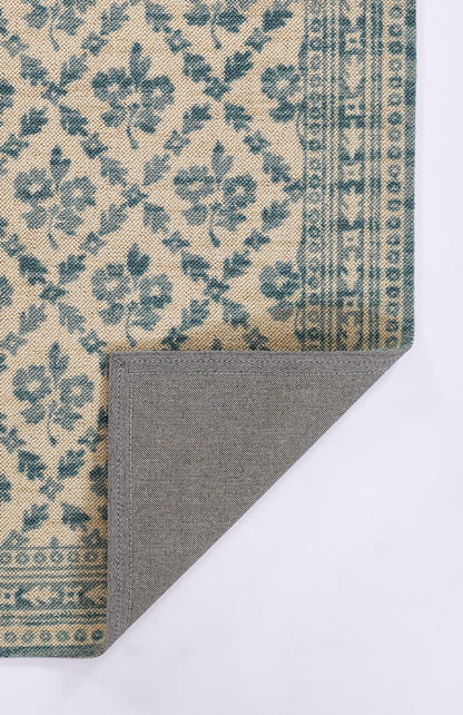 Beige rug with blue floral pattern and border; folded corner reveals grey herringbone backing.