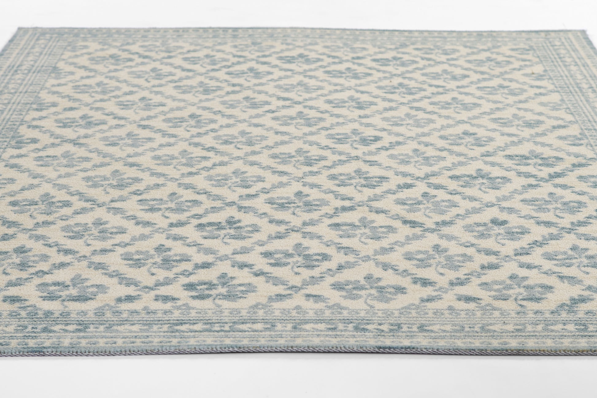Beige rug with bluish-gray lattice diamond floral pattern and decorative border.