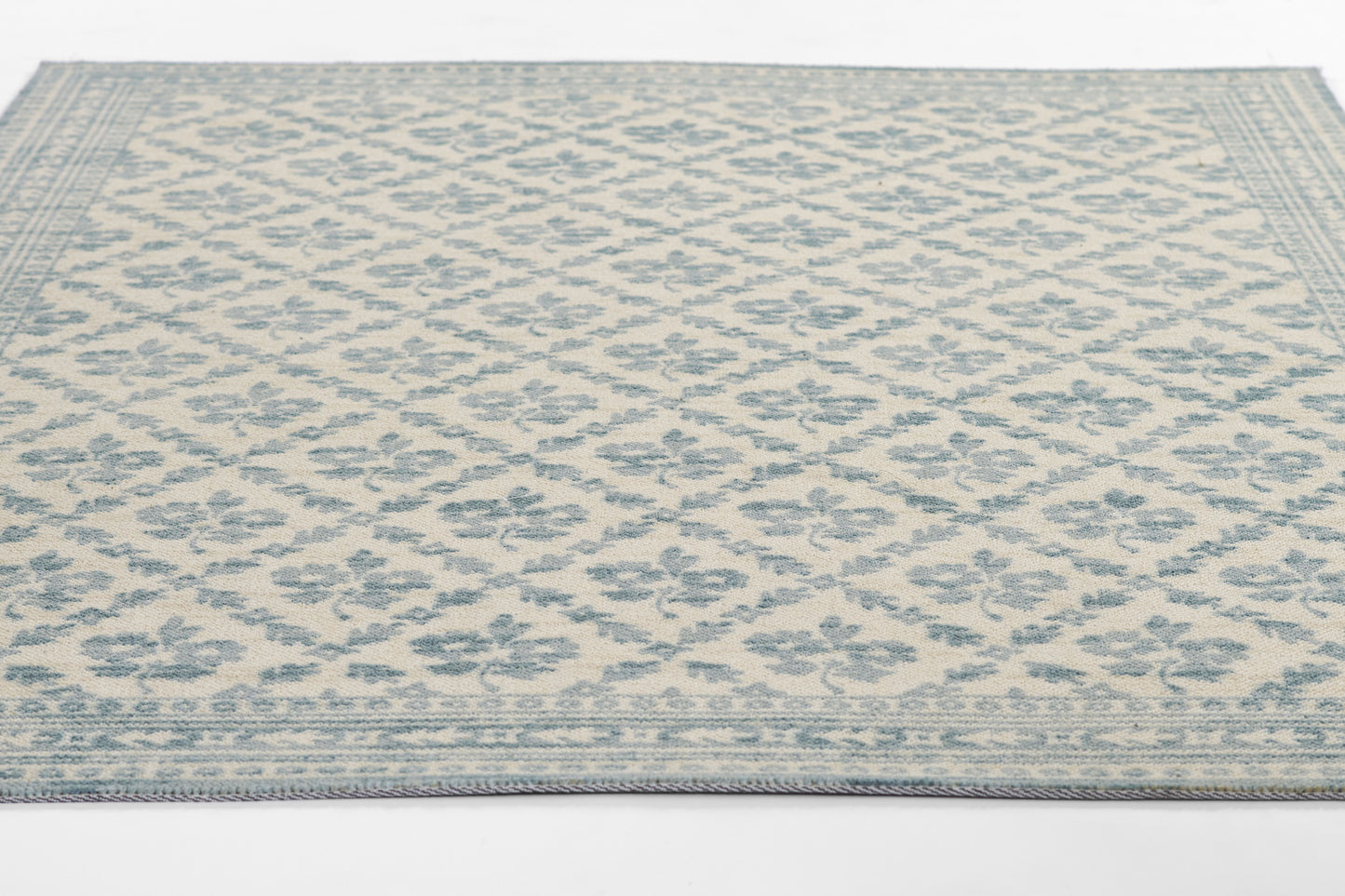 Beige area rug with a soft blue floral lattice pattern and a bordered edge.