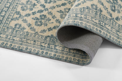 Blue-green and beige oriental area rug with floral border; folded corner reveals gray backing.