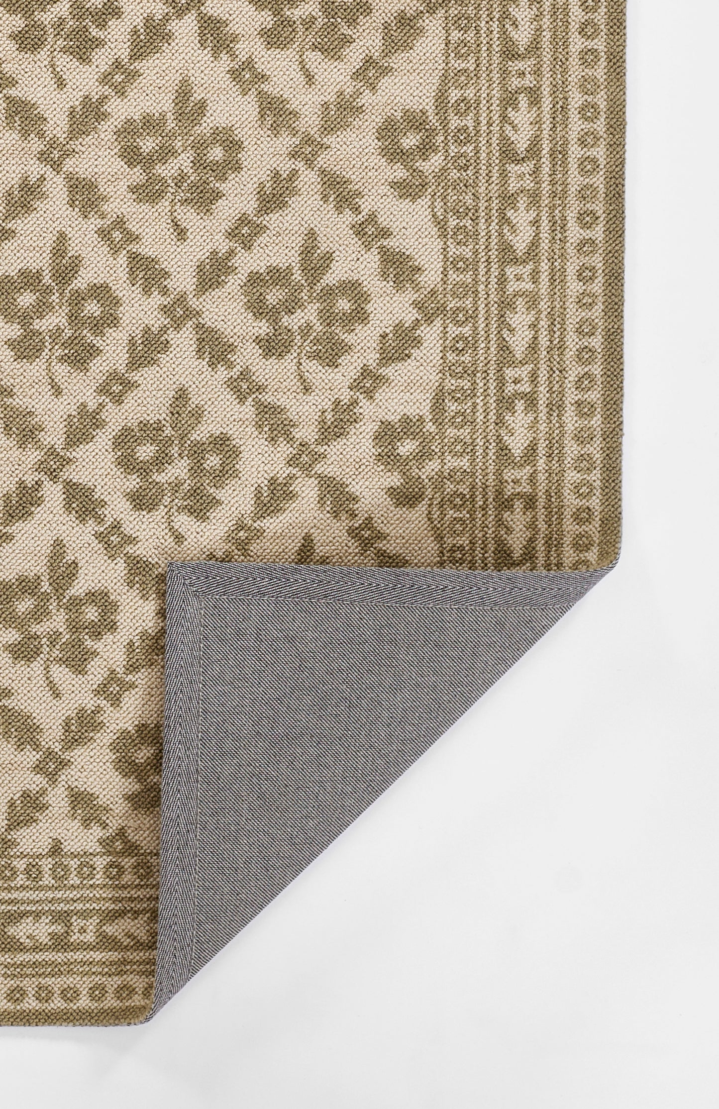 Beige and brown patterned area rug with floral motif and border; corner folded to reveal blue-gray herringbone backing.