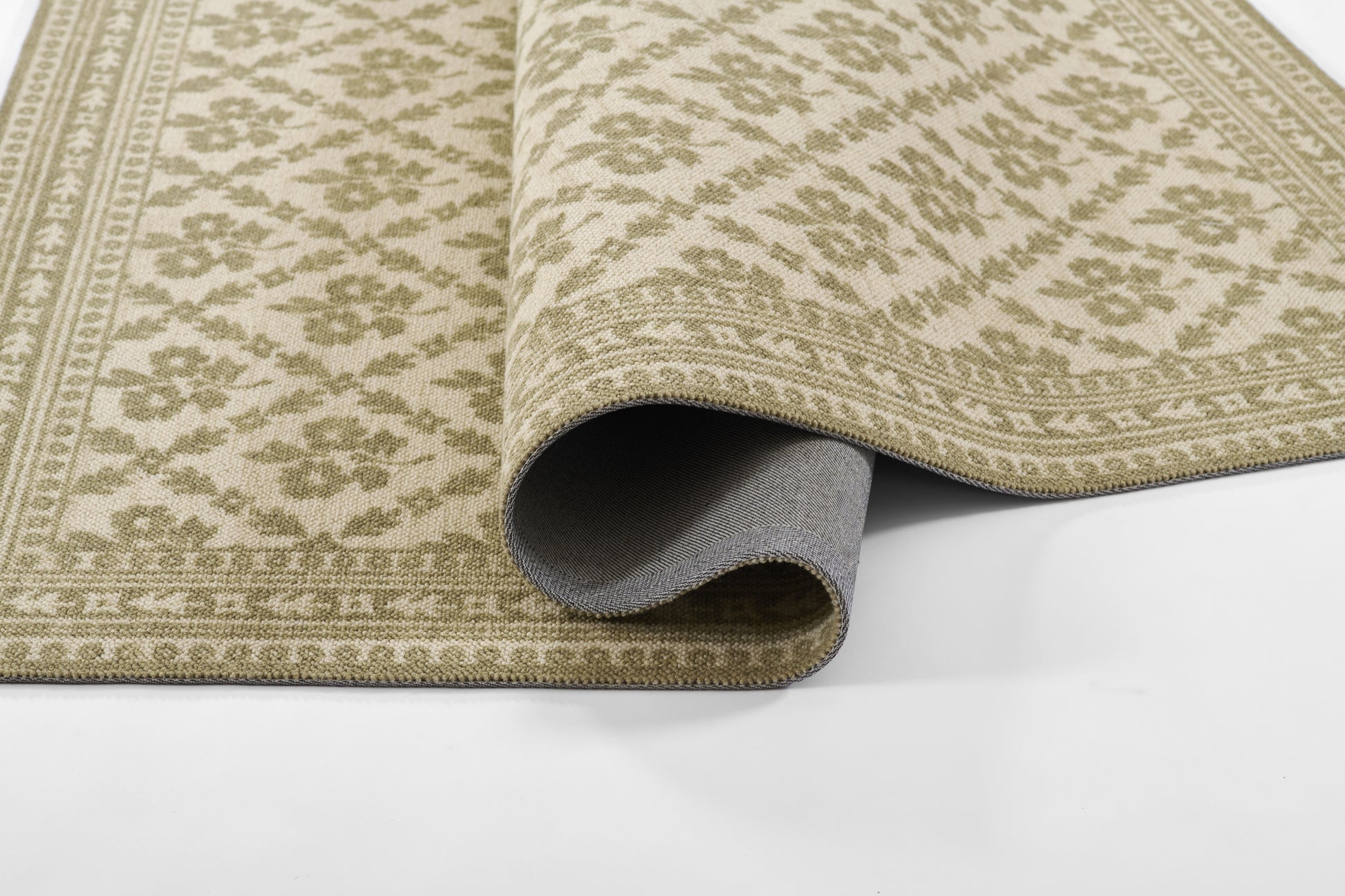 Beige and sage green patterned area rug with ornate border, woven texture, partially rolled at the edge.