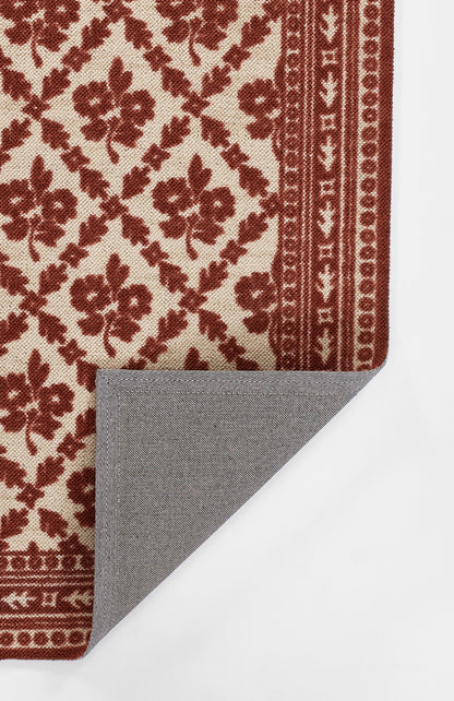 Red floral patterned rug on cream background with an ornate border; gray herringbone backing visible at the corner.