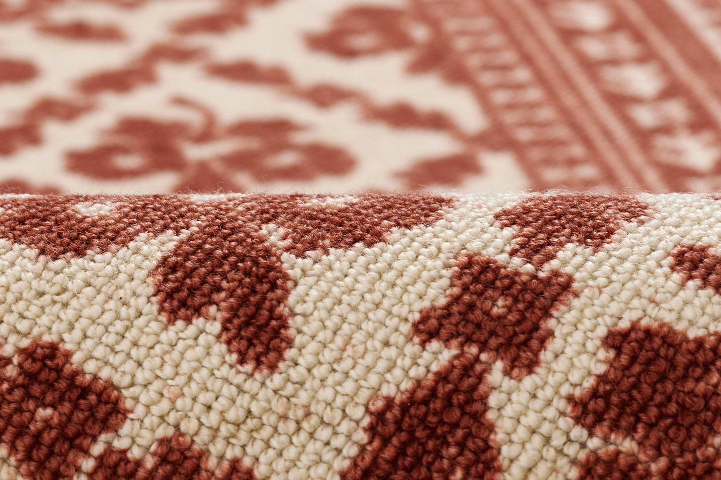 Close-up of a tufted rug with cream background and red geometric pattern, folded edge visible.