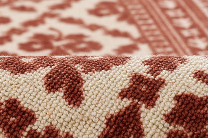 Close-up of red and cream woven rug with geometric floral pattern; tufted loop pile, rustic Persian-inspired design.