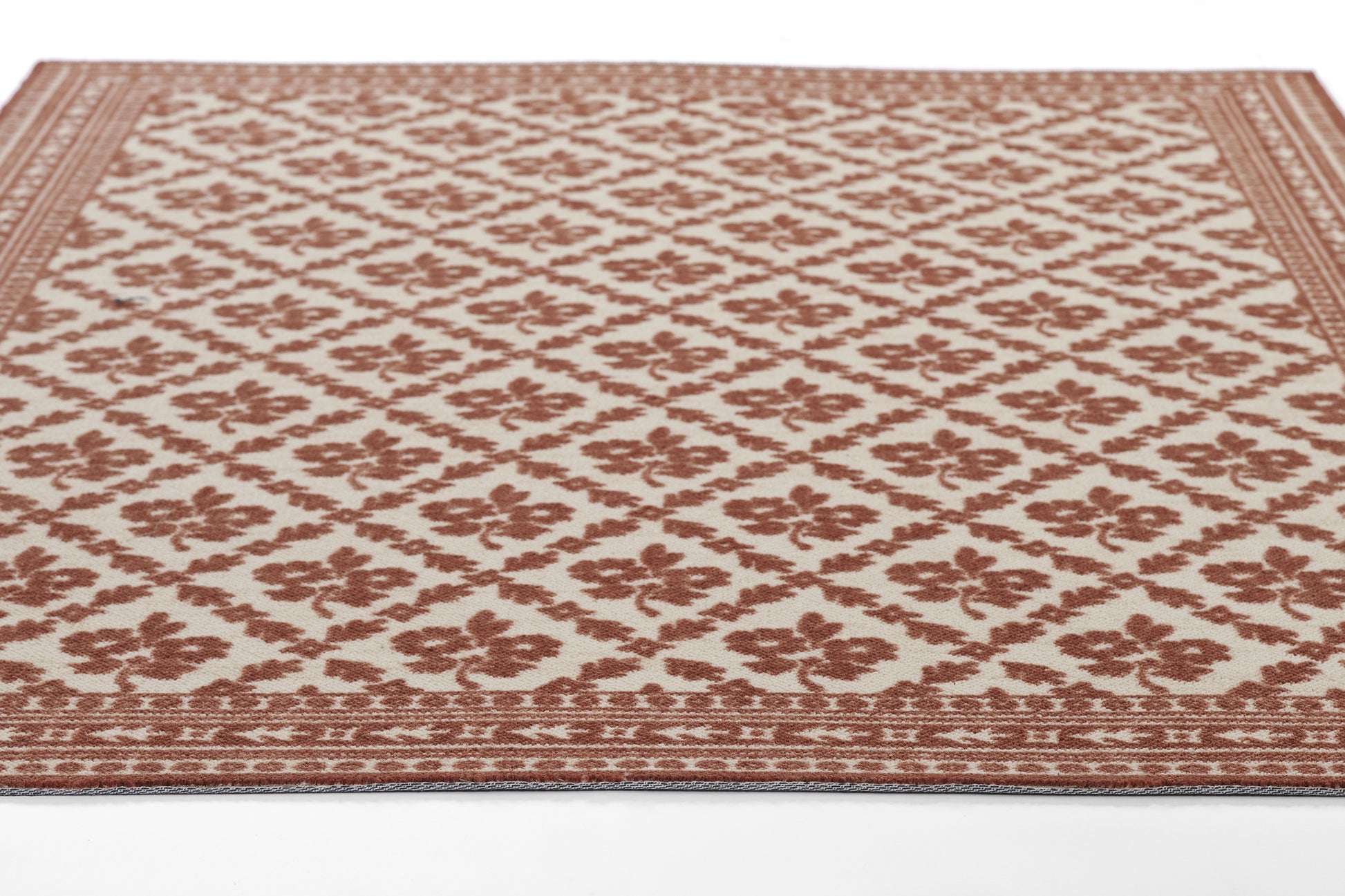 Rectangular rug in beige with reddish-brown diamond lattice floral pattern and decorative border.