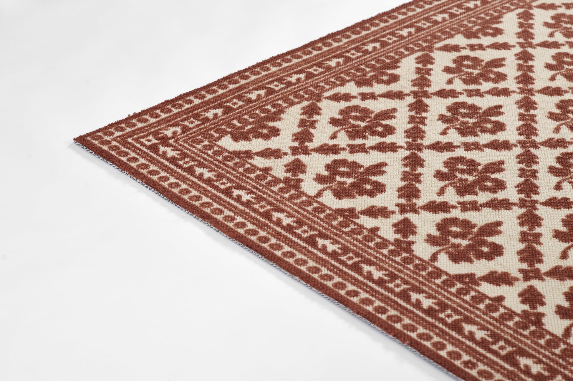 Beige area rug with red-brown geometric floral pattern and decorative border, angled corner view.