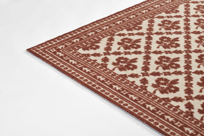 Beige area rug with red-brown geometric floral pattern and decorative border, angled corner view.