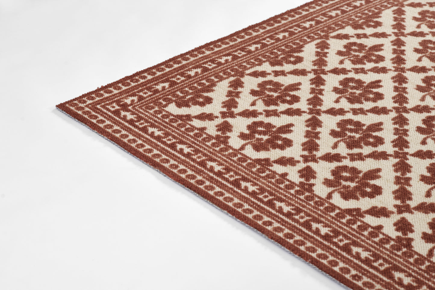 Rectangular woven rug with cream background and red-brown geometric floral motif; ornate border, vintage style.