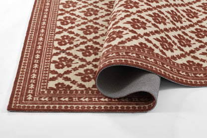 Rust-red and cream oriental rug with floral motif and ornate border, shown partly rolled to reveal gray backing.