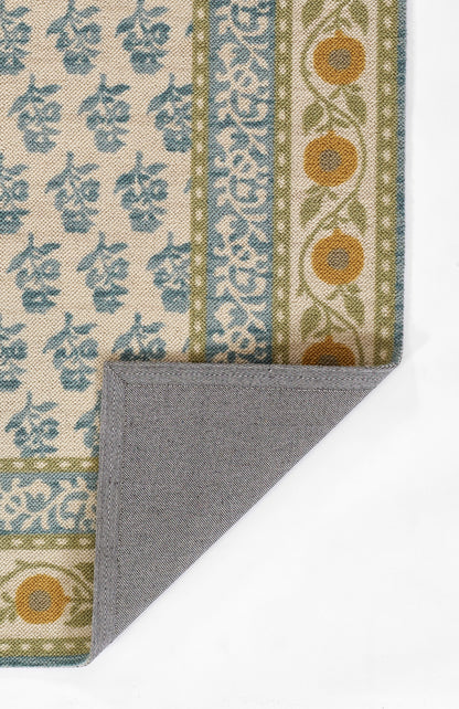Blue floral patterned rug on beige with blue-green border and orange circles; folded corner shows grey herringbone underside.
