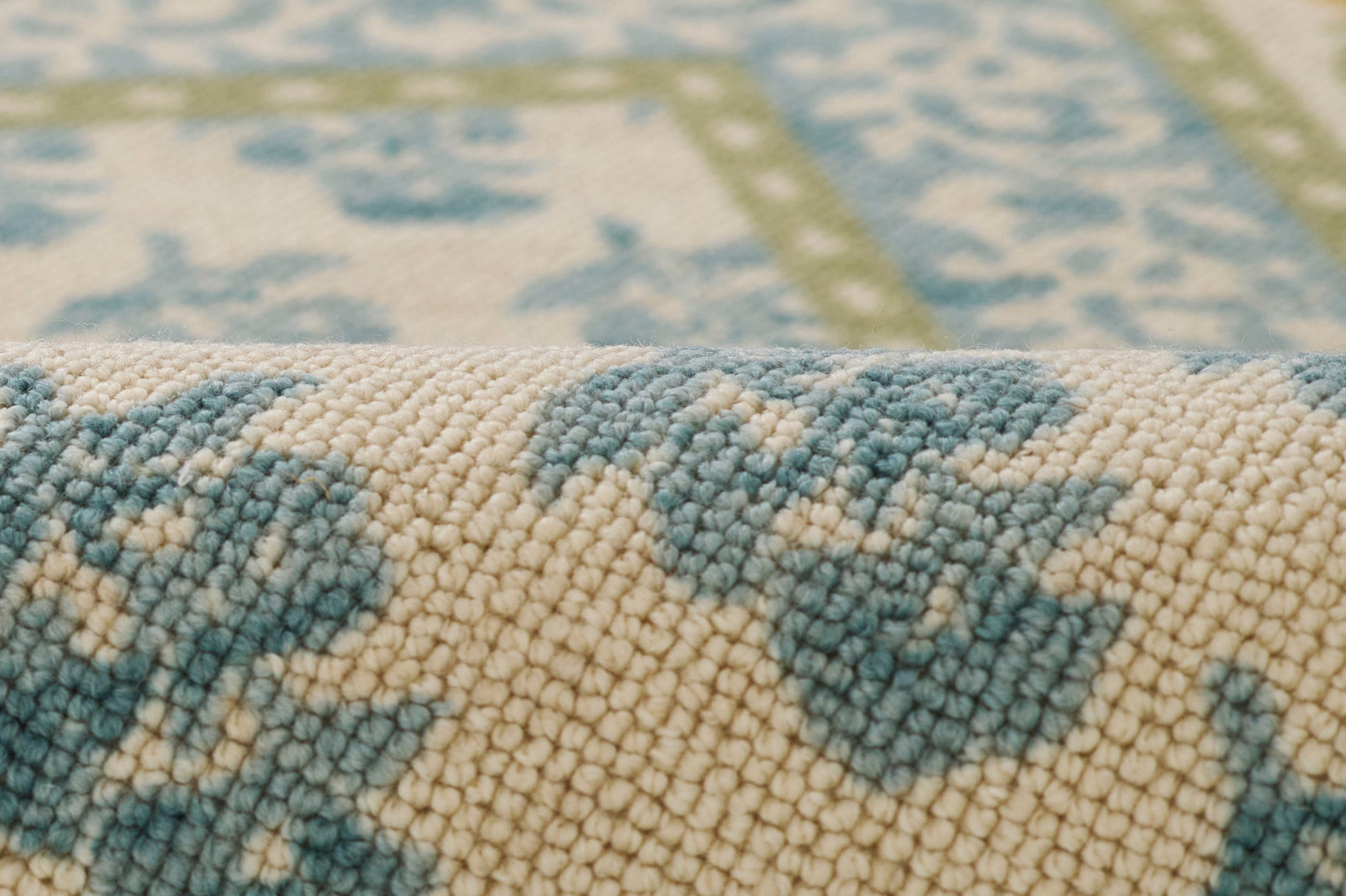 Close-up of a cream and blue woven rug with floral motifs, soft pile, and a rolled edge.