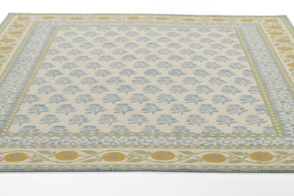 Area rug with light cream background, pale blue floral lattice center, blue inner border, and yellow-gold circular border motifs.