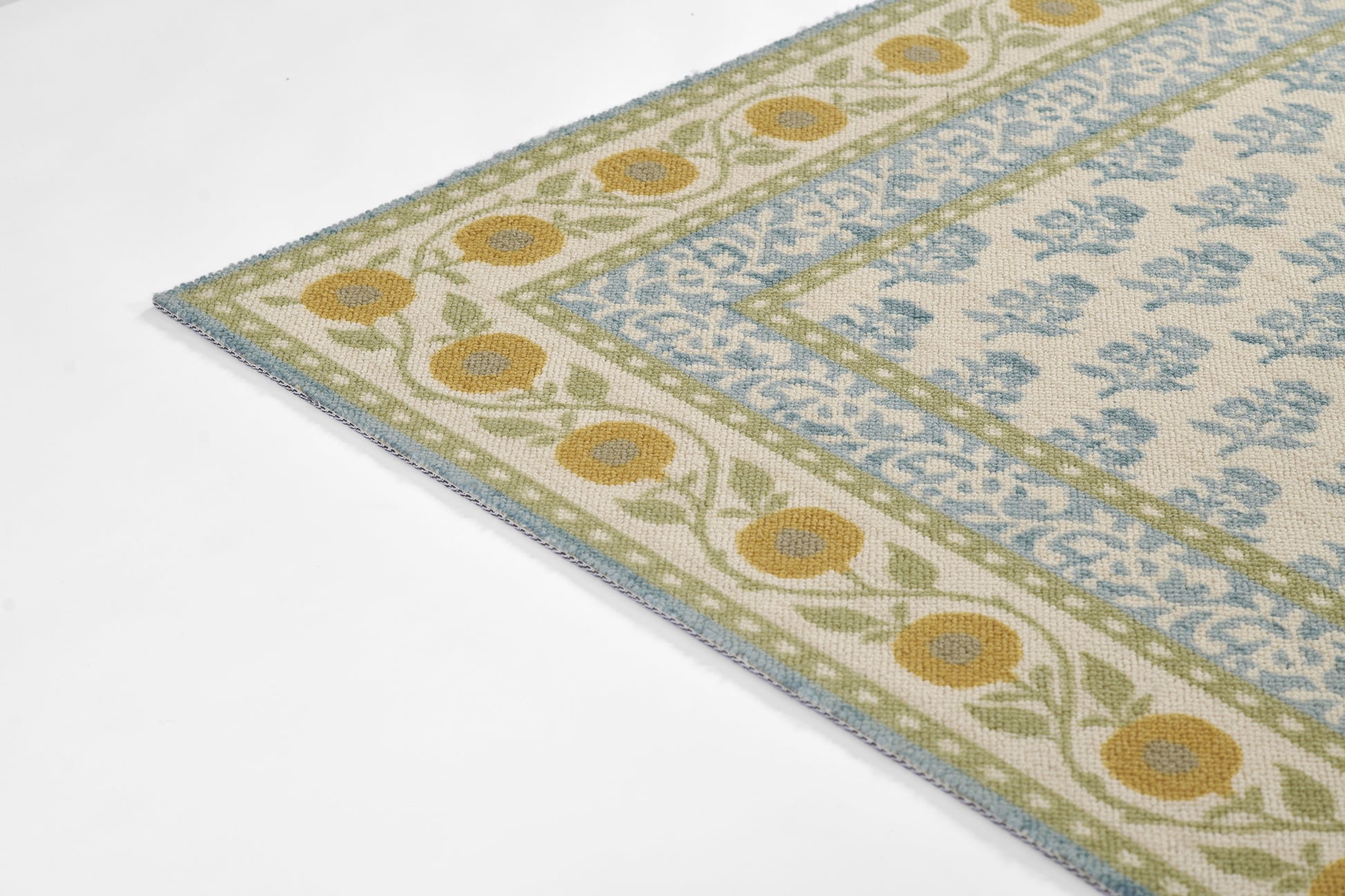 Rectangular woven rug with cream base, blue floral lattice center, olive-green border & yellow flower border; light blue edge.