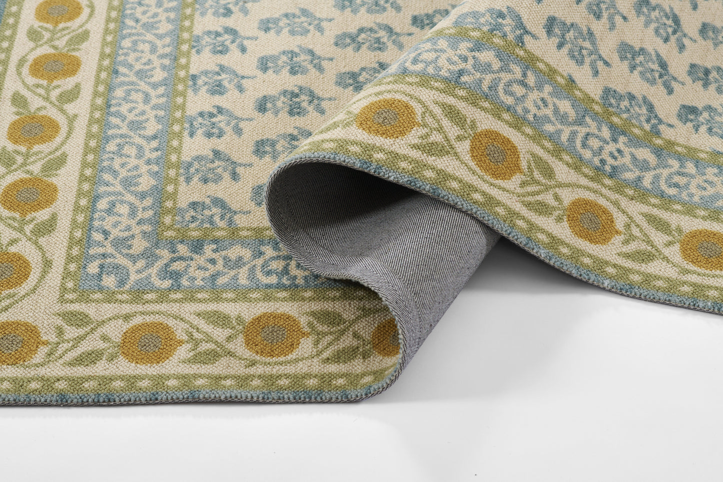 Patterned area rug with blue, green and yellow floral border on cream; rolled corner reveals gray backing.