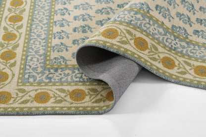 Woven area rug with beige field, blue floral border and green vine details; rolled corner shows gray backing.