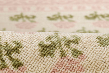 Cream woven rug with pink floral pattern and olive-green leaves, soft loop-pile texture.