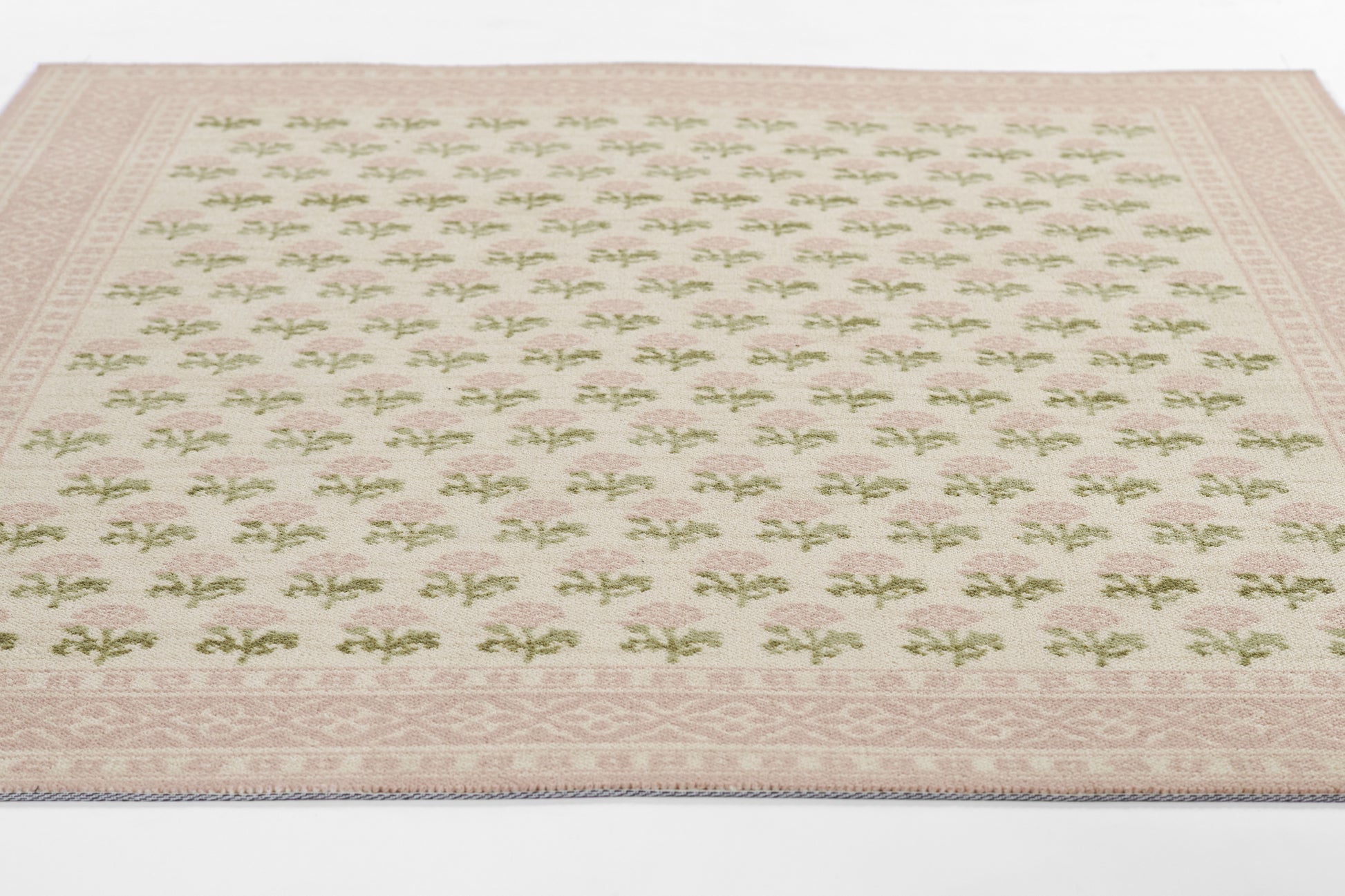 Cream rug with pink border and repeating green floral motifs; decorative border trim.