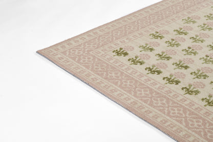 Soft pink and cream woven rug with geometric border and green floral motifs; flat-weave kilim style
