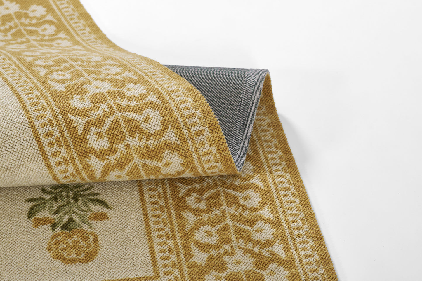 Gold and cream woven rug with ornate border and pineapple motif, folded to reveal gray back.