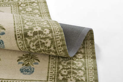 Beige and olive-green oriental rug with intricate floral border and blue blossoms; folded corner reveals gray underside.