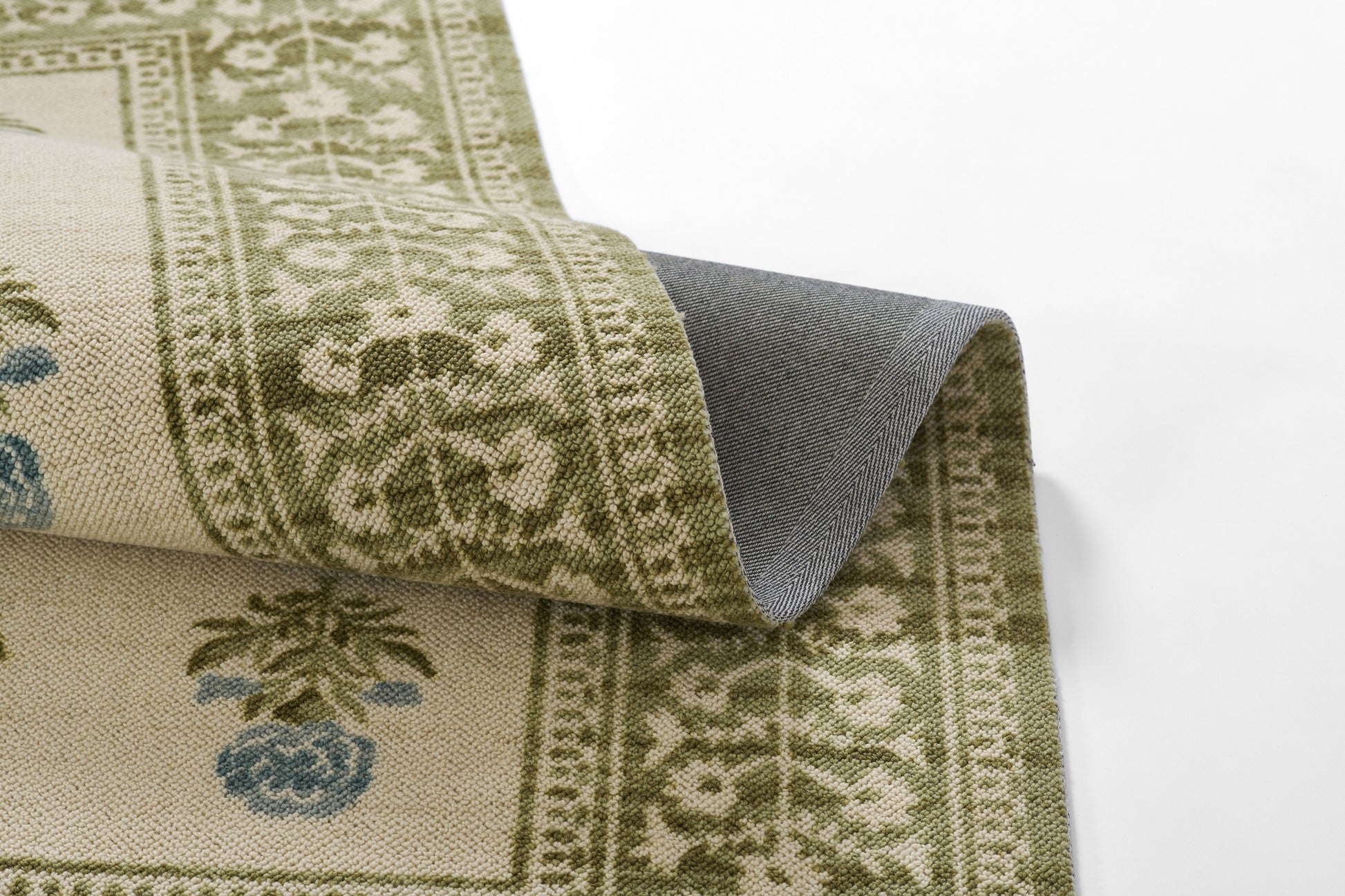 Beige and olive-green patterned rug with floral border and palm motif; curled corner reveals gray underside.