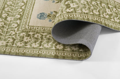 Olive-green woven oriental-style rug with beige and blue floral motifs, rolled to show gray underside.