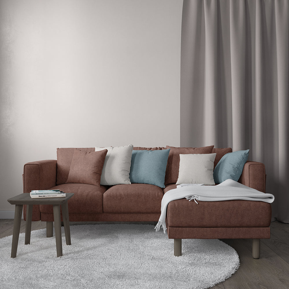 Rust velvet fabric upholstery with solid color & textured weave; shown on a sectional in a living room with blue/white/gray pillows, gray throw, round wood coffee table & light rug.