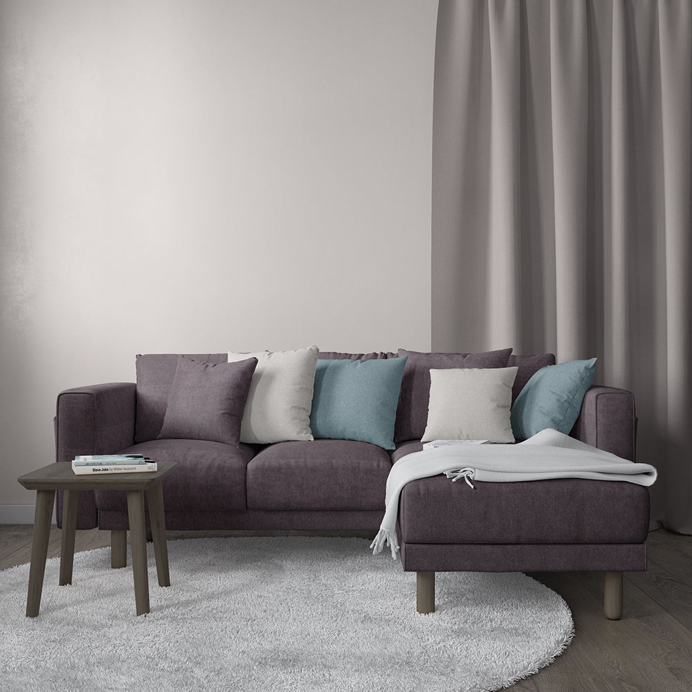 Purple sectional sofa with chaise, throw pillows in gray, teal and white, light gray rug, wooden side table, gray blanket.
