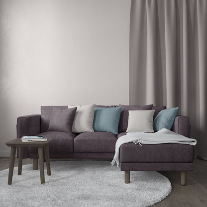 Purple sectional sofa with chaise, throw pillows in gray, teal and white, light gray rug, wooden side table, gray blanket.