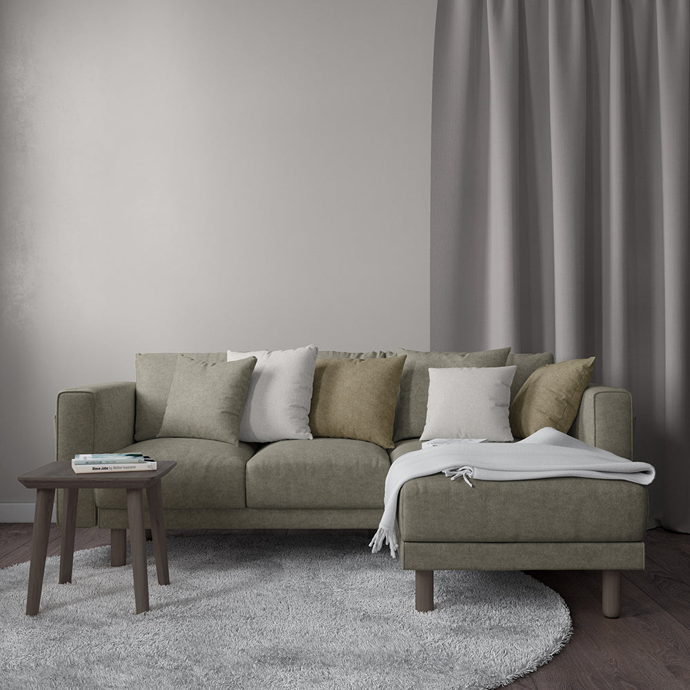 Putty velvet fabric – solid, textured – shown in a neutral living room setting with an olive-gray sectional with chaise, a gray rug, and a wooden side table with books.