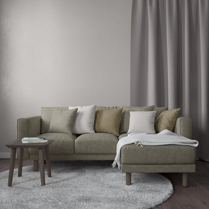 Putty velvet fabric – solid, textured – shown in a neutral living room setting with an olive-gray sectional with chaise, a gray rug, and a wooden side table with books.