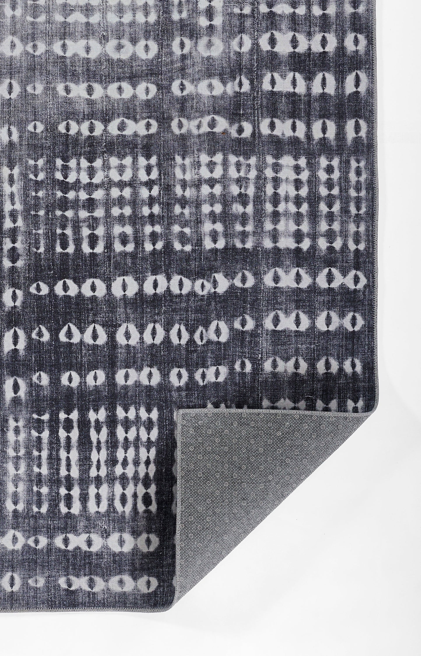 Dark navy rug with white circular dot lattice pattern; woven texture, corner folded to reveal gray non-slip underside.