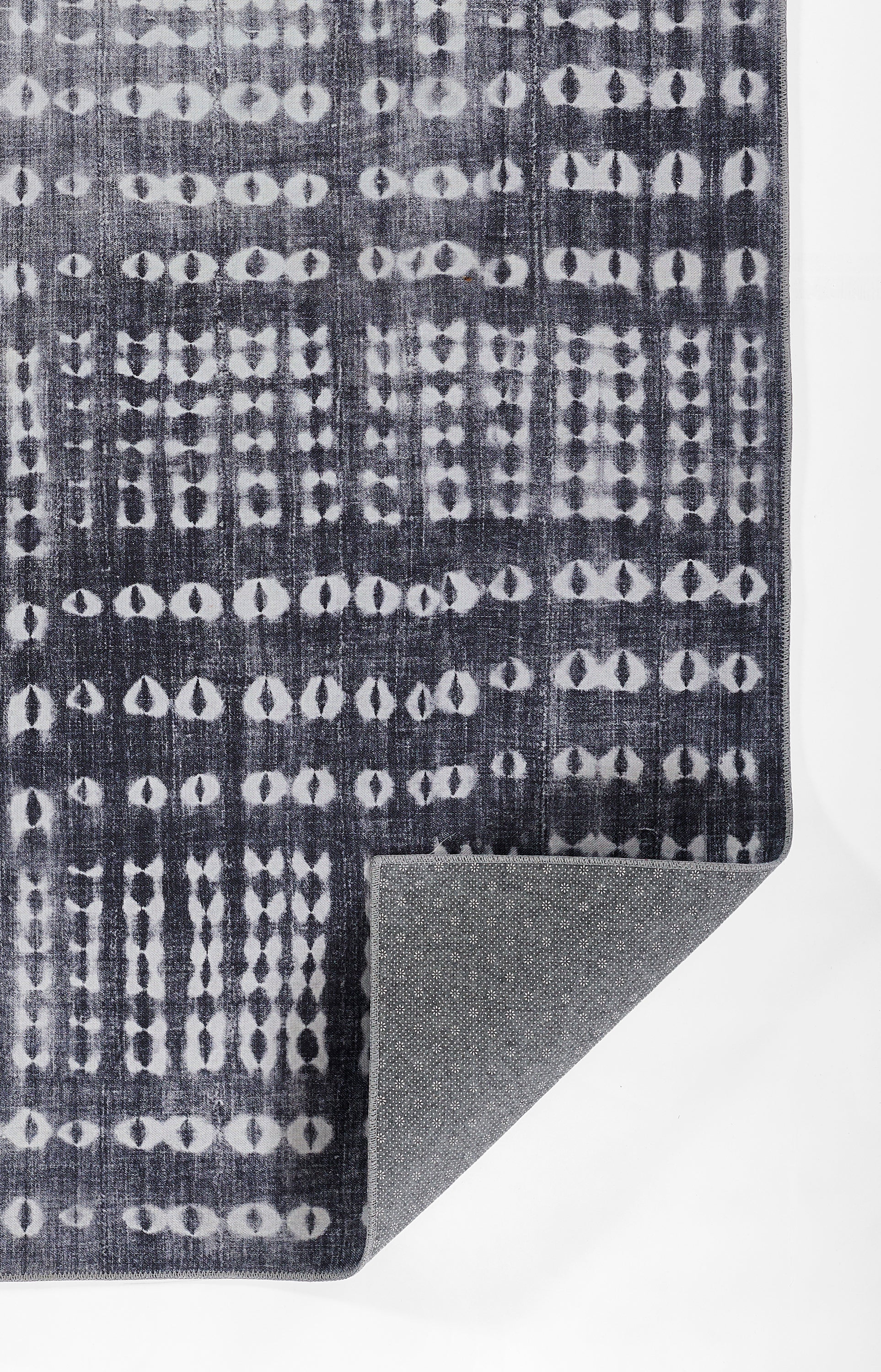 Dark navy rug with white circular dot lattice pattern; woven texture, corner folded to reveal gray non-slip underside.