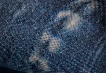 Close-up of dark blue denim fabric with light faded spots and visible twill texture.