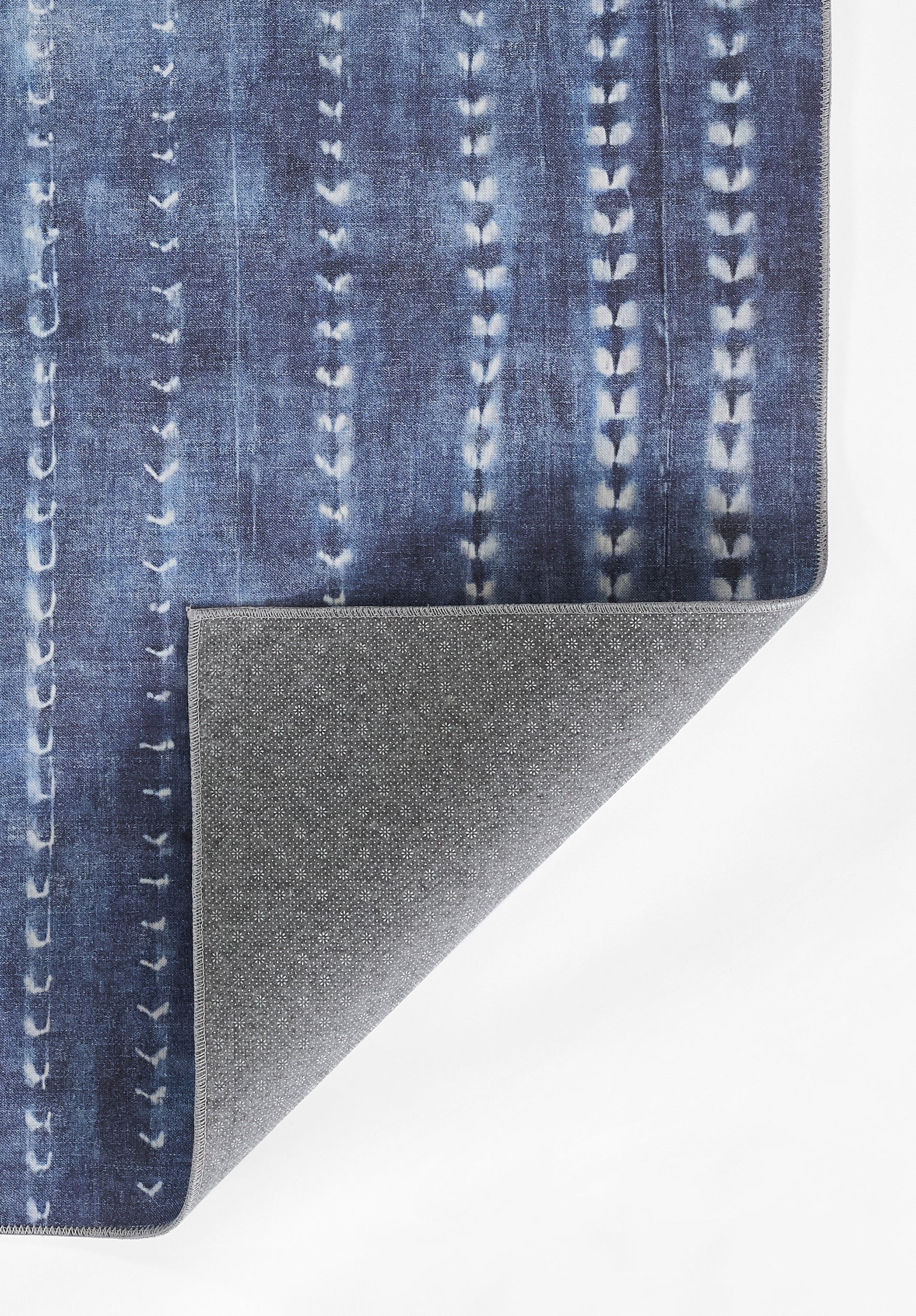 Blue denim-patterned rug with vertical stitched stripes; folded corner shows gray speckled non-slip backing.