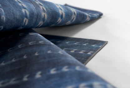 Blue denim rug, rolled and folded, with small white geometric marks on indigo weave.